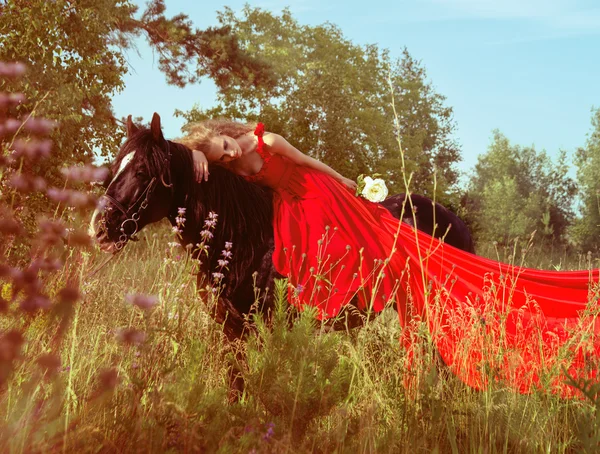 Mulher loira bonita em vestido vermelho no cavalo preto — Fotografia de Stock
