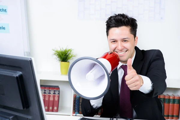 Businessman in an office, shouting on a megaphone, shows thumb u — Stock Photo, Image