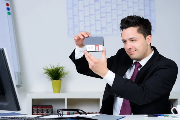 Happy businessman with a house model in the office — Stock Photo, Image