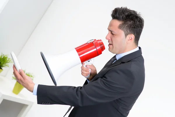 Angry businessman in an office, shouting on a megaphone, holding — Stock Photo, Image