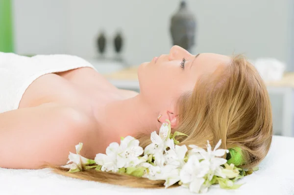 Beautiful woman wrapped in a towel laying in spa with white flow — Stock Photo, Image