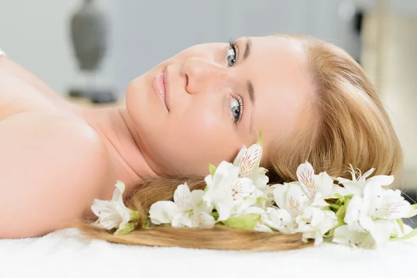 Beautiful woman wrapped in a towel laying in spa with white flow — Stock Photo, Image