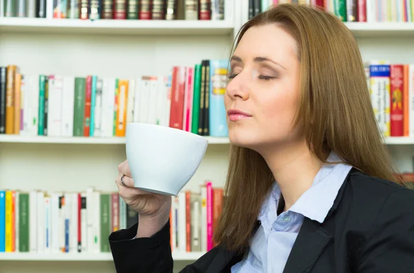 Junge Geschäftsfrau sitzt auf dem Schreibtisch mit Tasse — Stockfoto