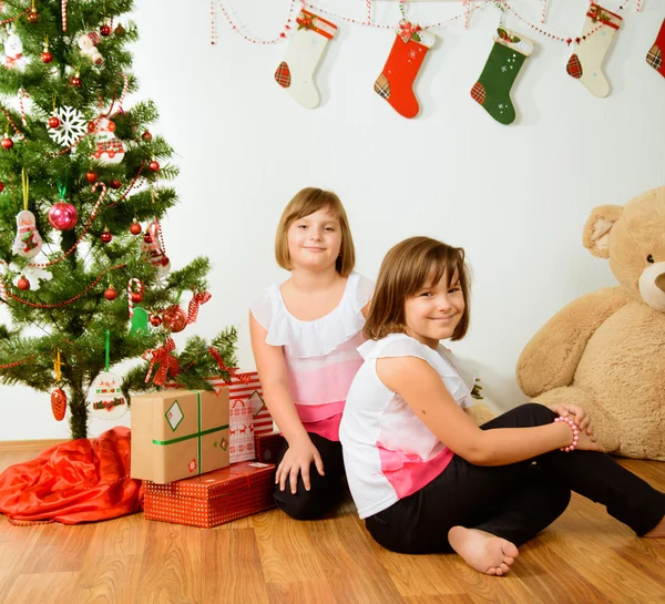 Two girls in front of christmas tree with gifts — Stock Photo, Image