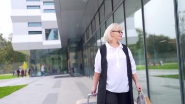 Dış binanın arka planında dizüstü bilgisayarı ve telefonu olan kendine güvenen çekici iş kadını portresi yakın plan. Yaşlı bir kadın profesör ya da öğretmen kameraya bakar ve gülümser.