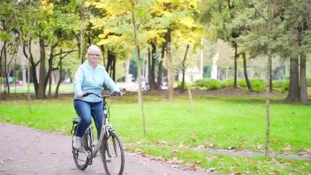 Šťastná seniorka jezdí na kole v parku a užívá si života. Stará cyklistka s retro motorkou stráví aktivní zdravý život v přírodě. Procházka podzimním lesem nebo městským parkem mimo.
