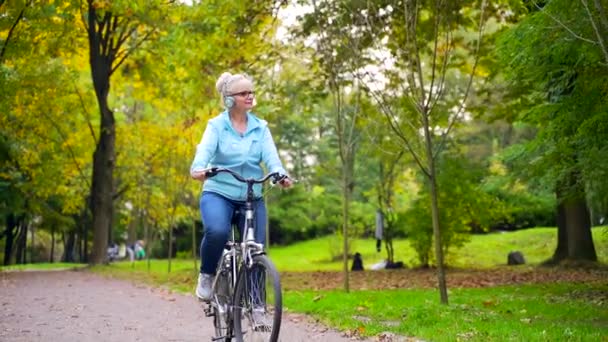 Счастливая Пожилая Женщина Наушниках Садится Велосипед Слушает Музыкальную Аудиокнигу Старая — стоковое видео