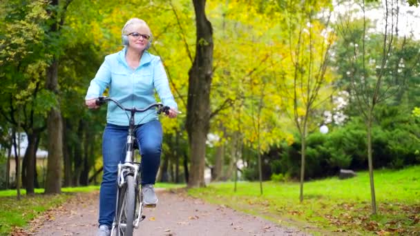 Ευτυχισμένη Ηλικιωμένη Γυναίκα Ακουστικά Παρκάρει Ένα Ποδήλατο Και Ακούει Μουσική — Αρχείο Βίντεο