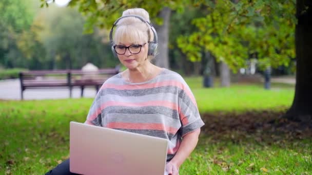 Mujer Moderna Edad Avanzada Auriculares Césped Mirando Ordenador Portátil Escuchando — Vídeos de Stock