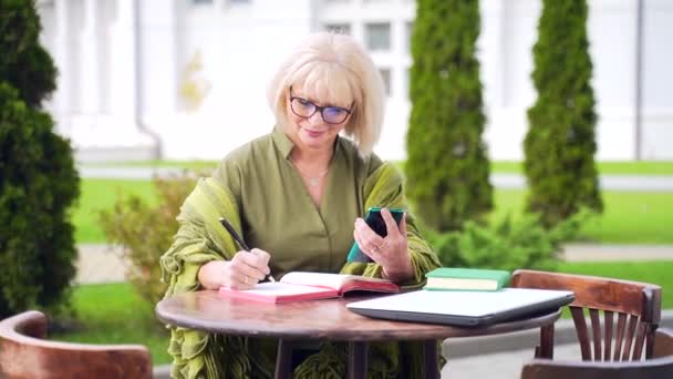 高级商业女性会计使用电话笔记本和笔记本电脑处理文档 外面桌子边的女商人很忙 五十岁的女经理在银行业工作 — 图库视频影像