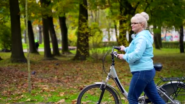 Vrolijke Seniorenvrouw Met Bril Loopt Met Een Fiets Het Park — Stockvideo