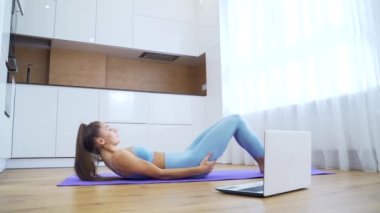 Kilitleme faaliyetleri. Milenyum kızı antrenman videolarını takip ediyor. Evde dizüstü bilgisayarla eğitim gören güzel bir genç kadın. Yoga, pilates, egzersiz.