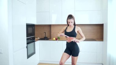 İnce vücutlu ve spor giyimli ince beli olan genç bir fitness kadının portresi mutfakta bantla bel çevresini ölçüyor. Çekici atletik kız arka planda ölçü alıyor.. 