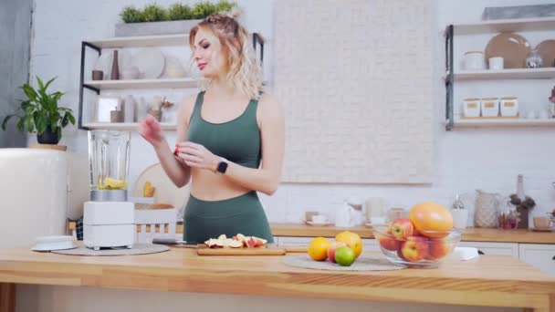 家のキッチンで健康的なスムージーや新鮮な果物の朝食を作るためのブレンダーで果物をスケッチ若いスポーティ女性の肖像画 ワークアウトの後に健康的な朝食を準備フィットネスの女の子 — ストック動画