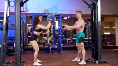 İki fitness erkeği ve kadın spor kulübünde ya da spor salonunda birlikte çalışırlar. Çift bir topla çömelme egzersizi yapıyor. Ortak eğitim. Sporcu antrenörü ya da antrenör antrenörleri ısınma egzersizleri yapar