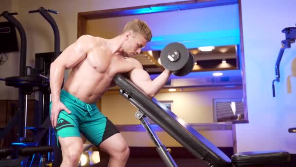 在体育俱乐部或体育馆里 年轻的健美男子赤身裸体的健美运动员手拿哑铃或杠铃训练二头肌 强壮的家伙在训练机器上做二头肌运动 白种人男性 — 图库视频影像