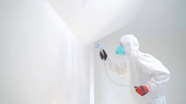 Havasız sprey boya. Duvarı havasız sprey tabancayla beyaza boyayan bir işçi. Arka, arka görüş. Deneyimli bir adam yüzeyine akrilik beyaz boya spreyler mekanik bir hava aracı ile