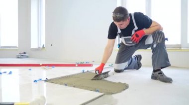 Beton zemine seramik bir fayans döşeyen inşaat onarımı için alet ve yapıştırıcı kullanılıyor. İşçi tamirci ustası, çentik mala vuruyor fayans yapıştırıcı ve çentik mala karışımı