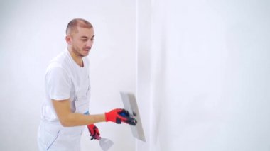 Tecrübeli bir tamirci duvarları sıva ile kaplıyor, spatula, macun bıçağı ve modern havan topu ve sıva kullanıyor. Portre profesyoneli macun sıva. Usta zanaatkar, uzman beyaz yüzey yapıyor.