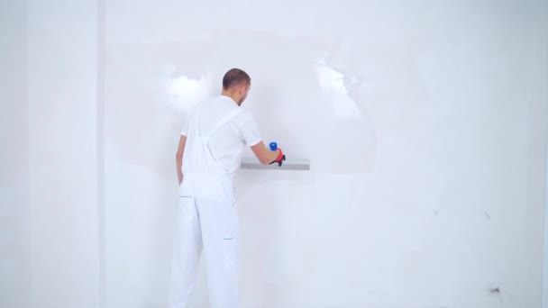 経験豊富な修理工は パテナイフと白の近代的なモルタルを使用して 漆喰壁です 肖像プロの男パテ石膏 熟練した職人専門家が白い表面を作り — ストック動画