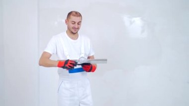 Deneyimli bir tamirci, elinde bir spatula, macun bıçağı kaplama. Profesyonel portre sanatçısı macun ustası, uzman kameraya bakar ve arka plandaki beyaz duvara gülümser.