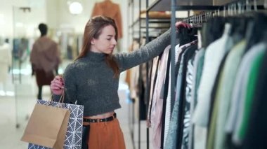 Genç bayan alışverişçi alışveriş merkezindeki bir raftaki kıyafetleri inceliyor. Moda mağazasından alışveriş yapan bir kadının portresi. Kara Cuma 'da kıyafet indirimini seçer ve ona dokunur. Hoş ve çekici bir kız.