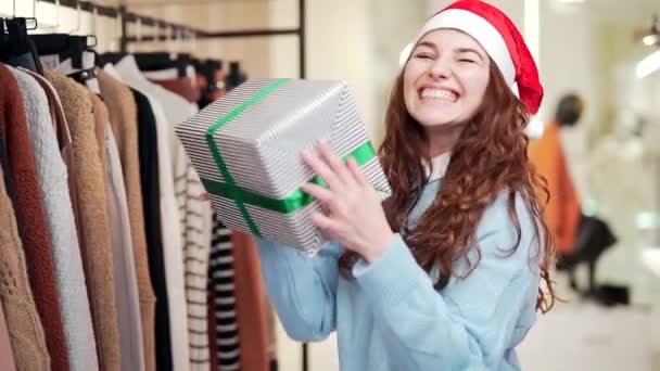 在商场里 滑稽的女销售经理头戴圣诞礼帽 头戴礼品盒跳舞 在服装店的新年大减价 快乐快乐的女人摆姿势拍照 冬季销售 — 图库视频影像