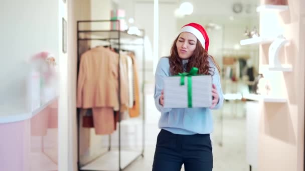 在商场里 滑稽的女销售经理头戴圣诞礼帽 头戴礼品盒跳舞 在服装店的新年大减价 快乐快乐的女人摆姿势拍照 冬季销售 — 图库视频影像