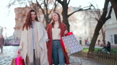 İki mutlu genç kadın soğuk sonbahar ya da bahar mevsiminde ellerinde hediye çantalarıyla şehir sokaklarında alışveriş yaptıktan sonra alışveriş merkezlerinde ya da mağazalarda iki neşeli kız dışarı çıkar.