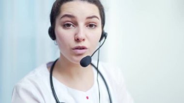 Kadın sıhhiyeci videosu danışman hastayı arıyor. Webcam görüntüsü. Kadın doktor, kameranın web kamerasına bakarak sanal sohbette uzaktan tıbbi yardım sağlayan kulaklık takıyor. Teletıp