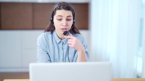 閉じる若い女性は 電話会議で通信ヘッドセットを着用自宅のオフィスでコンピュータを見て話すビデオチャットジョブインタビューやオンライン教師との距離言語コースクラス女性のラップトップ — ストック動画