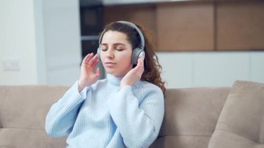 Evdeki kanepede dinlenip kablosuz kulaklık takarak müzik dinleyen güzel öğrenci kız. Çekici genç bir kadın oturma odasında dinleniyor. Gözleri kapalı bir şekilde kanepede yatıyordu..