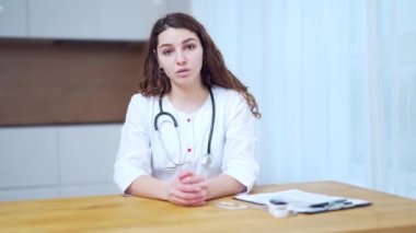 Profesyonel kadın doktor kameraya bakıp konferans görüntüsü alıyor. Web kamerasıyla konuşan kadın hekim uzaktan kumandalı bir hastayla sohbet ediyor.