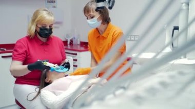 Kıdemli kadın dişçi, bir diş kliniğinde kanalı modern ekipmanlarla dolduruyor. Kanallar mühürleniyor. Yeni yöntemler tedavi araçları dişler özel bir fotopolimer madde ile