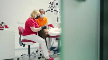 Kıdemli kadın dişçi, bir diş kliniğinde kanalı modern ekipmanlarla dolduruyor. Kanallar mühürleniyor. Yeni yöntemler tedavi araçları dişler özel bir fotopolimer madde ile