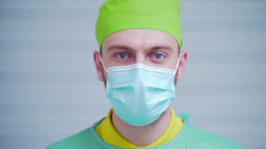 Yüz portresi, genç yakışıklı erkek doktor, cerrah, dişçi, pediyatrist, şapkalı bir maske. Hastanedeki ya da diş muayenehanesindeki kameraya bakan mavi gözlü hoş bir doktor.