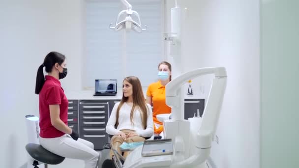 若い女性歯科医は 治療や現代の歯科クリニックでの手順を開始する前に 患者に話します 秘書の専門医がオフィスで女性の相談について説明します — ストック動画