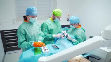  Diş cerrahlarından oluşan bir ekip dişlerini ameliyat eder. Modern bir klinikte. Genç dişçi. Takım çalışması. Diş doktoru ortodontist cerrah kanal tedavisi yapıyor. Stomatoloji Ofisi