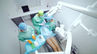 Diş cerrahlarından oluşan bir ekip dişlerini ameliyat eder. Modern bir klinikte. Genç dişçi. Takım çalışması. Diş doktoru ortodontist cerrah kanal tedavisi yapıyor. Stomatoloji ofisi. Üst görünüm