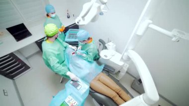 Diş cerrahlarından oluşan bir ekip dişlerini ameliyat eder. Modern bir klinikte. Genç dişçi. Takım çalışması. Diş doktoru ortodontist cerrah kanal tedavisi yapıyor. Stomatoloji ofisi. Üst görünüm