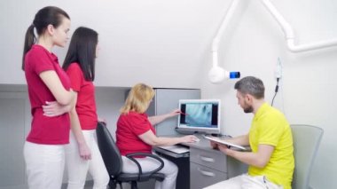 Tıbbi dişçi ekibi diş muayenehanesinde röntgen görüntülerini tartışıyor ve inceliyor. Modern diş kliniği x-ray odasındaki bilgisayar masaüstü ekranına bakıyoruz. 