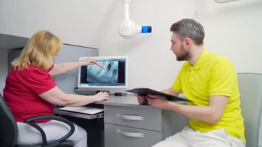 Tıbbi dişçi ekibi diş muayenehanesinde röntgen görüntülerini tartışıyor ve inceliyor. Modern diş kliniği x-ray odasındaki bilgisayar masaüstü ekranına bakıyoruz. 