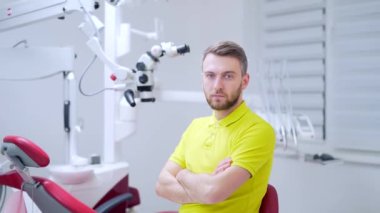 Kendine güvenen bir dişçinin tıbbi muayenehanedeki ya da klinikteki yakın plan portresi. Çekici sakallı genç adam, iş yerindeki modern erkek doktor ya da doktor. Hastanedeki kameraya bakıyorum.