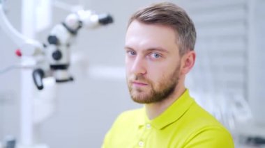 Kendine güvenen bir dişçinin tıbbi muayenehanedeki ya da klinikteki yakın plan portresi. Çekici sakallı genç adam, iş yerindeki modern erkek doktor ya da doktor. Hastanedeki kameraya bakıyorum.