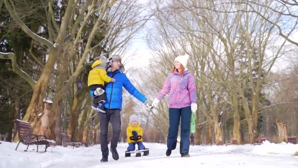 幸福的新婚夫妇 他们带着年幼的孩子 冬天背着雪橇在雪地的公园里散步 在周末 年轻的丈夫和妻子带着年幼的儿子在一起消磨时光 — 图库视频影像