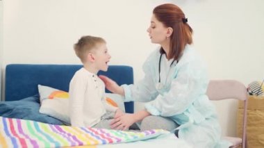 Dost canlısı, neşeli bayan çocuk doktoru evde bebeğin boğazını ve ağzını muayene ediyor. Aile doktoru küçük bir çocuğu muayene ediyor. Hasta çocuk kadın bir doktor tarafından muayene ediliyor.