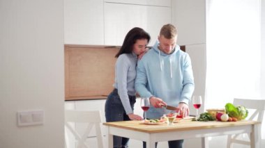 Genç evli çifti seven karı koca, modern mutfakta birlikte sağlıklı yemekler pişiriyor. Sebze salatası hazırlamak ve şarap içmek için birlikte zaman geçirin. Mutlu ve neşeli bir aile
