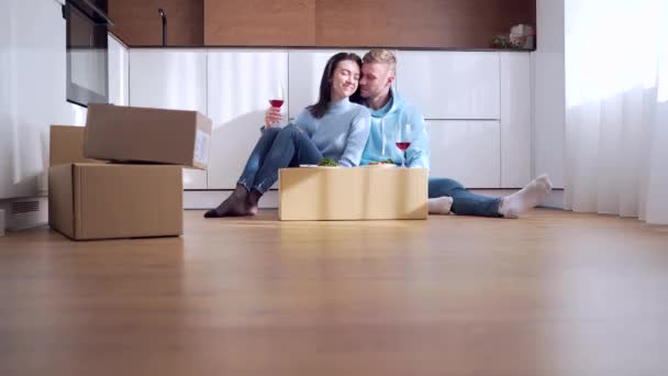 一对快乐的年轻夫妇在搬到家里的新公寓后 在一个纸板箱里的临时桌子上吃午饭 喝葡萄酒 新购买的住房 — 图库视频影像