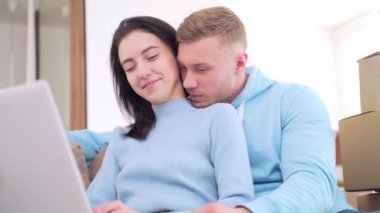 Mutlu genç aile alışverişi evdeki online mağazada. Yeni bir daire için. Çift evleri için mobilya ve aletleri internet ve kanepede oturan bir dizüstü bilgisayarla seçiyor..