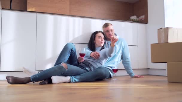 年轻快乐的已婚男女夫妻坐在地板上庆祝搬到新公寓或新家 他们喝酒 计划在纸板箱附近的内部 现代设计的梦想 — 图库视频影像